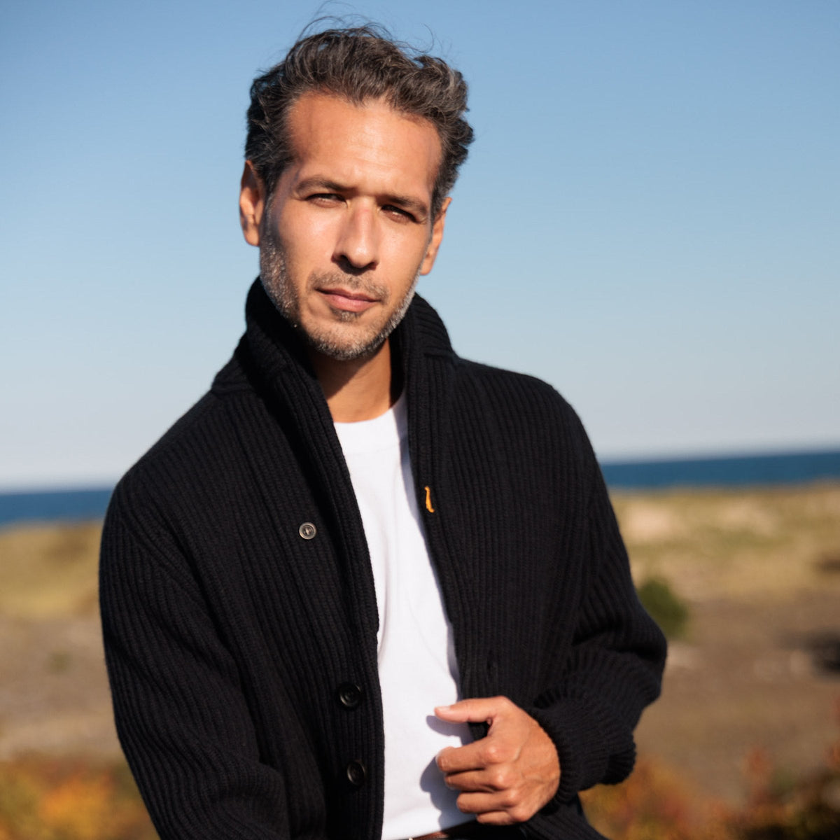 The Bruce 8-ply Scottish cashmere shawl collar cardigan in Matte Black, seated, full length
